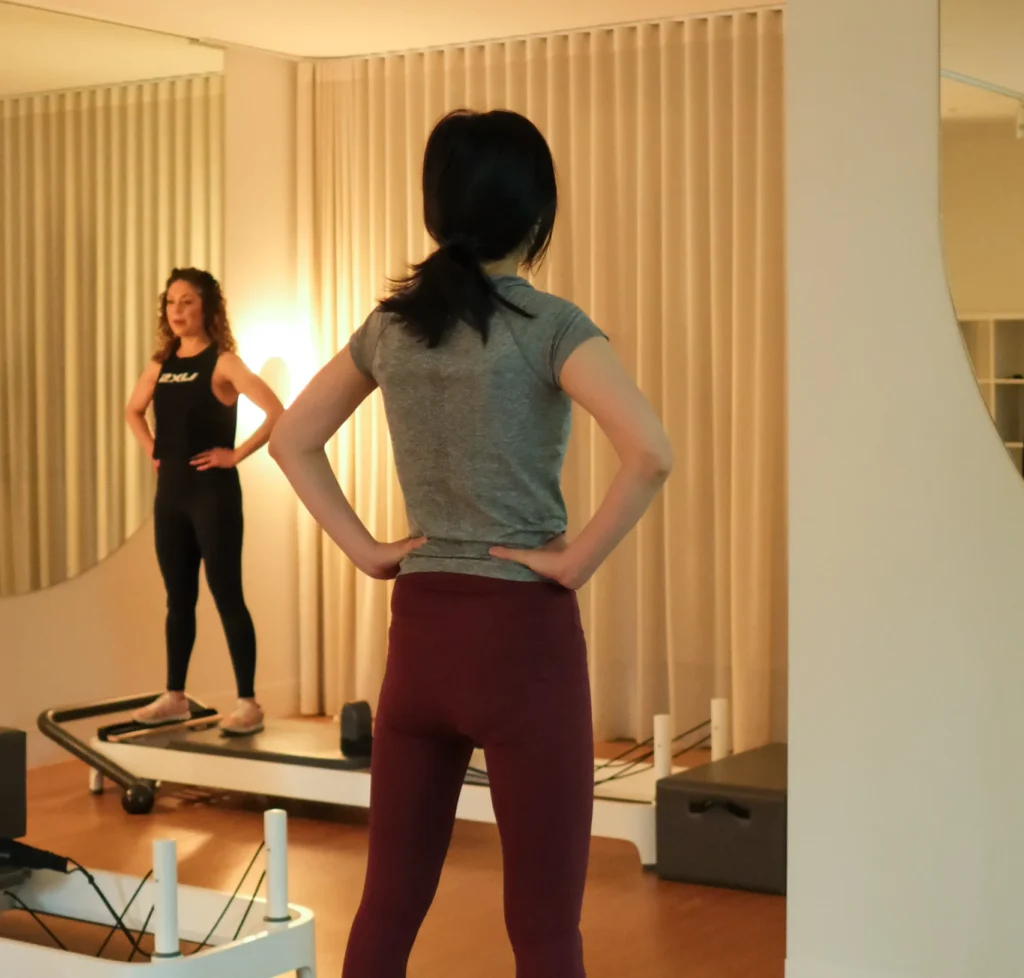 A pilates instructor assisting a student with a standing pilates exercise in a studio.